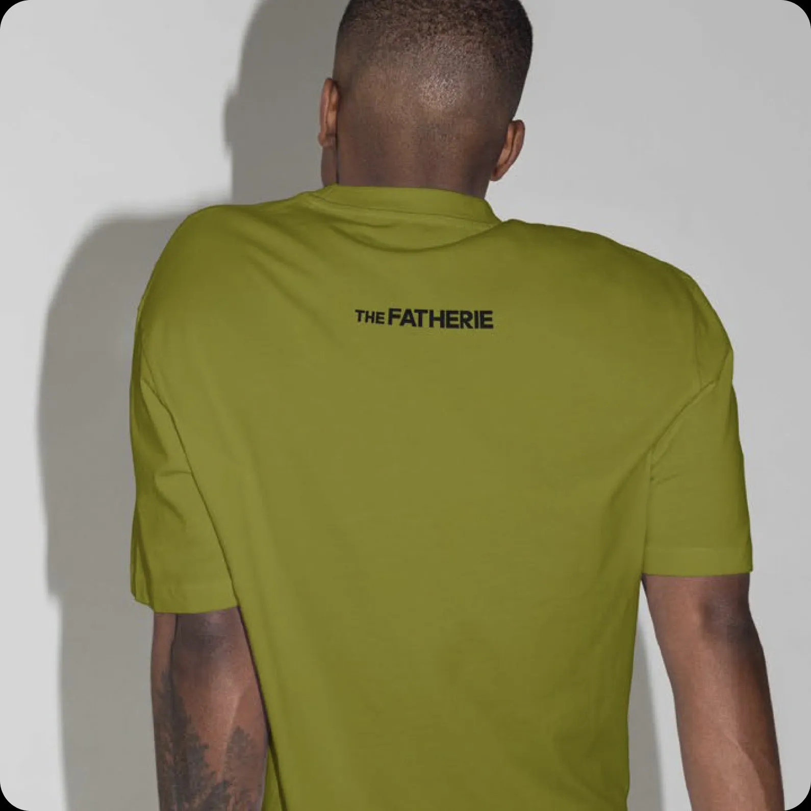 A man seen from behind in an olive tee with The Fatherie across the shoulders