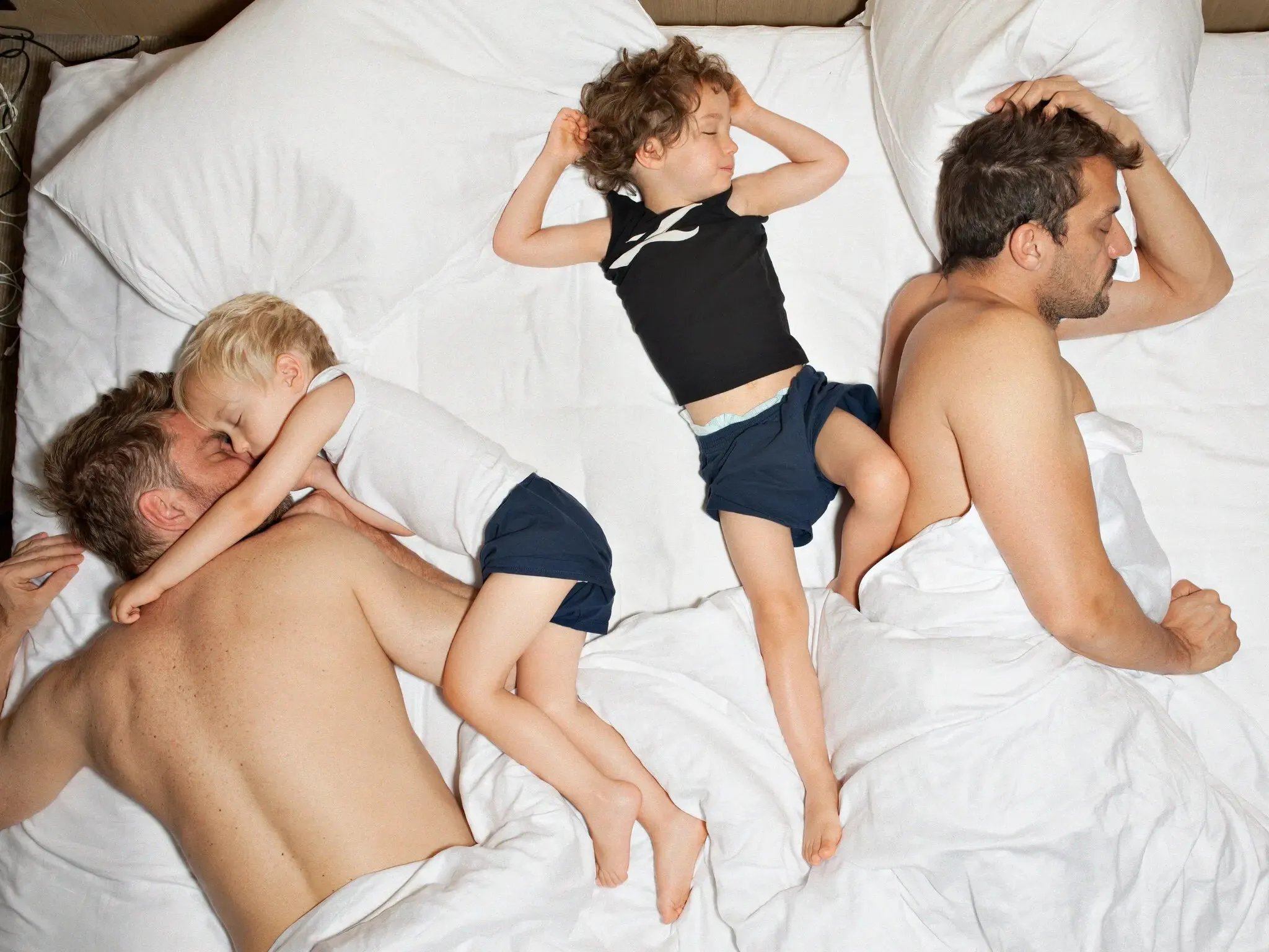 A father and two children asleep across a white bed, seen from above