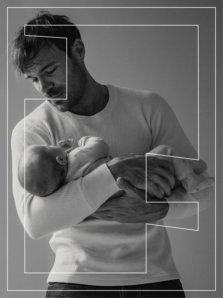 Black and white portrait of a father cradling his newborn, the Anvil mark framing them