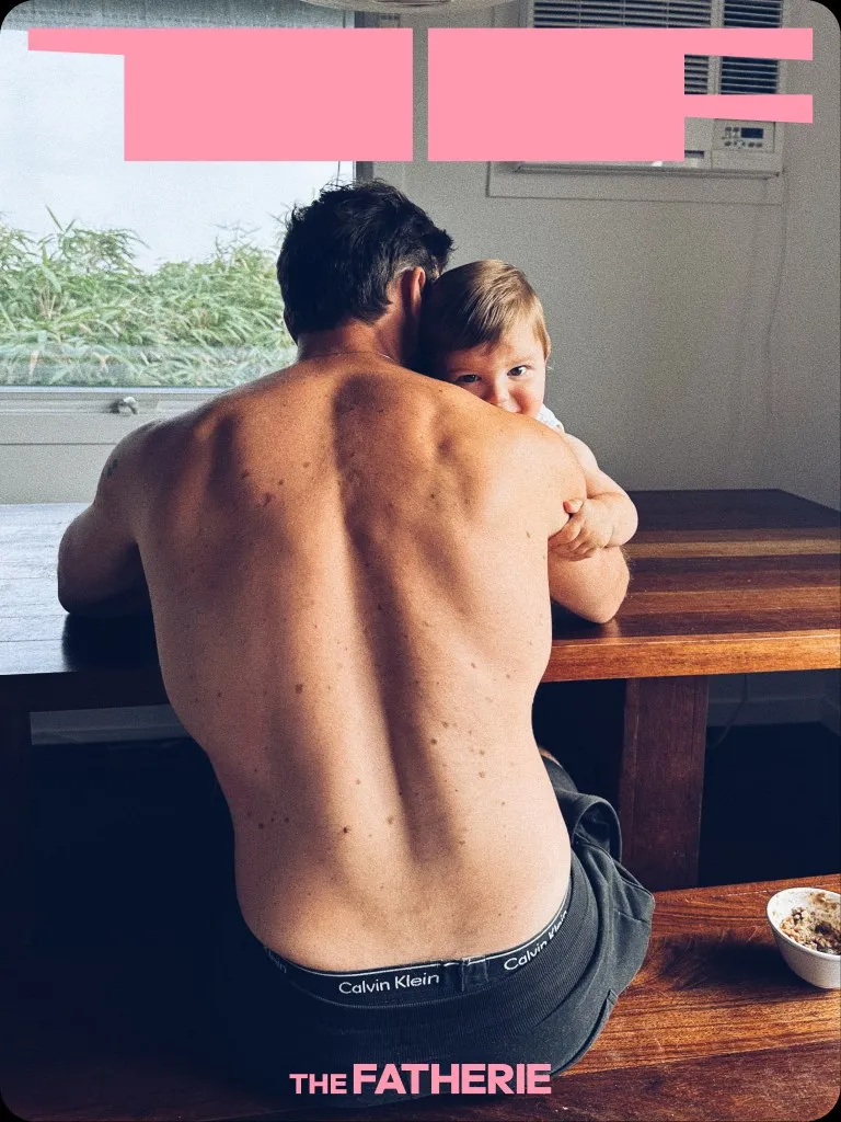 A father seen from behind at a table with his son on his shoulder