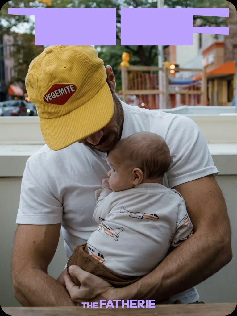 A father in a Vegemite cap holding his baby outside a café
