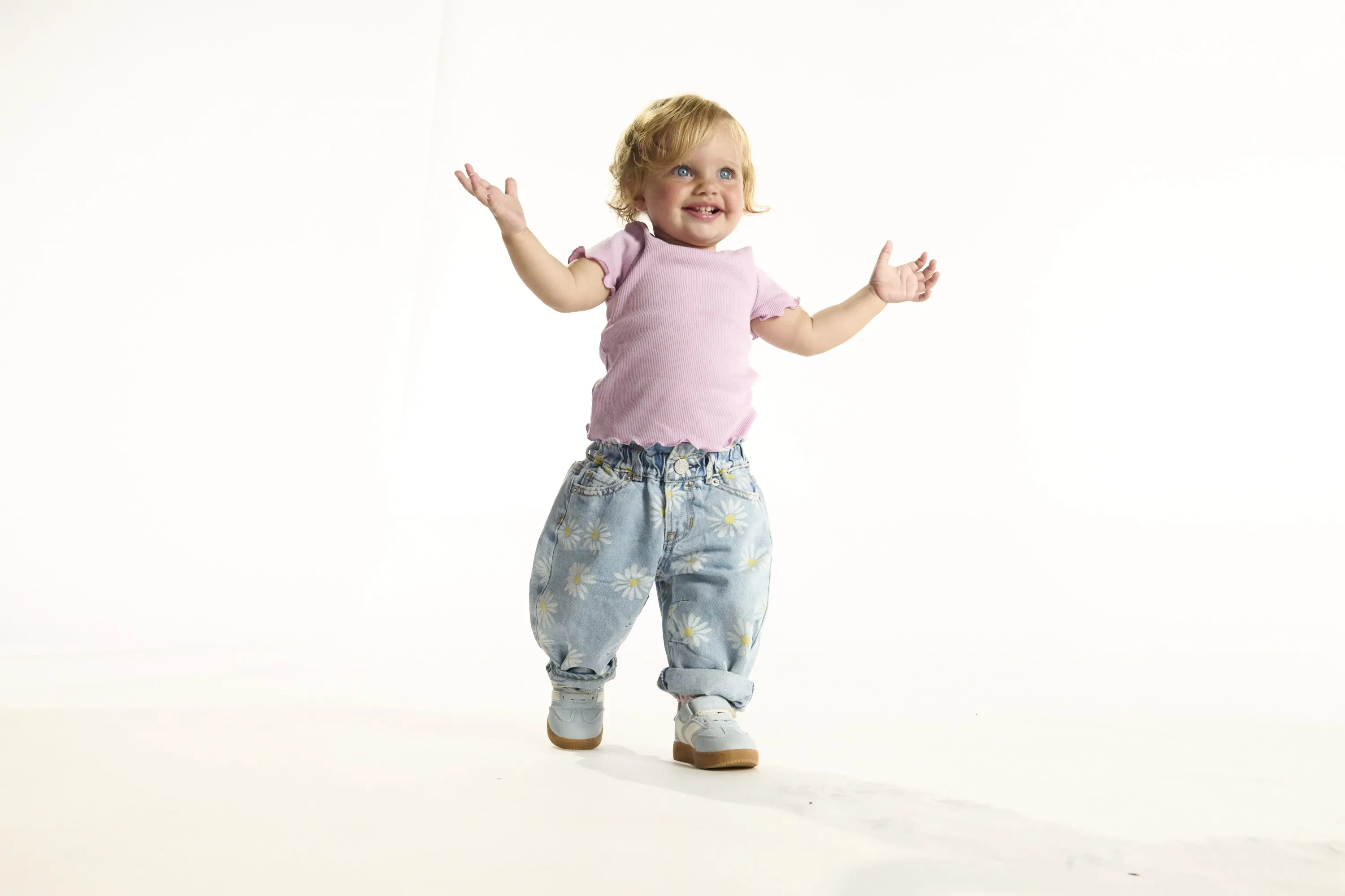 A toddler in a lilac top laughing with her arms thrown wide